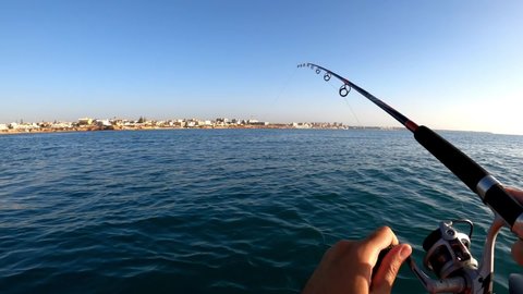 Mil Palmeras beach,Alicante, Spain, August 24, 2020: A sportsman fishing in kayak pulling out of water a fish hooked to a lure in mediterranean sea.