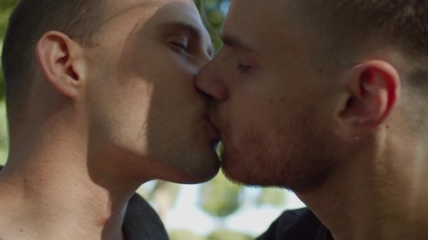 Lifestyle portrait of affectionate attractive homosexual couple with eyes closed kissing passionately, expressing love, tenderness and strong relationship while lovers spending time together outdoors.