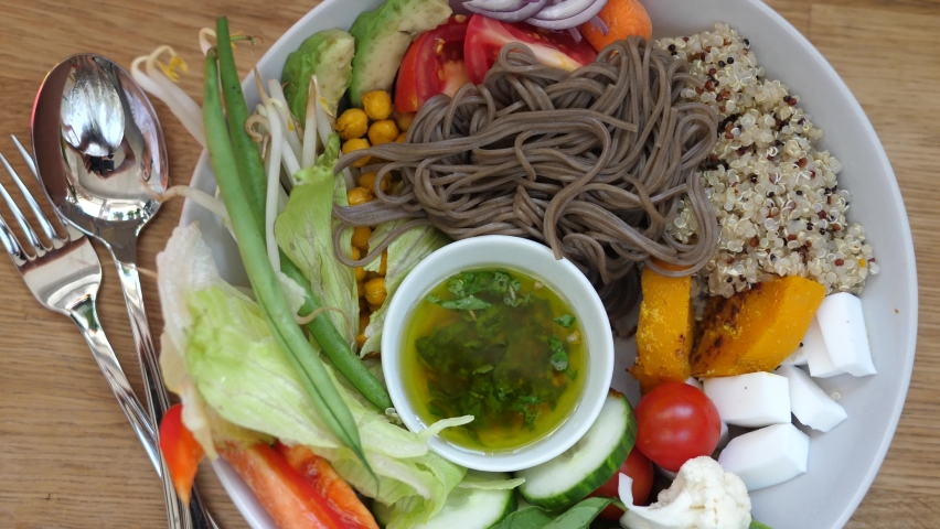 Top view of hand pouring dressing onto warm salad with soba noodles, quinoa and fresh vegetables. Balanced diet and healthy lifestyle | Shutterstock HD Video #1059714095