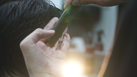 Close up view on cutting hair process in barbershop. Professional barber combing and cutting hair of male client. Hairdresser making trendy hairstyle. Concept of hair care. Slow motion