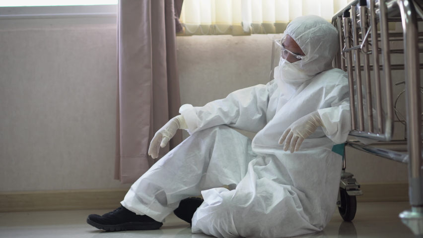 tired doctor wearing ppe suit take a break near bed after hard work feeling worry and sad  in operating room at hospital. exhausted and desperate  surgeon of Coronavirus pandemic  of covid 19 outbreak Royalty-Free Stock Footage #1059715727