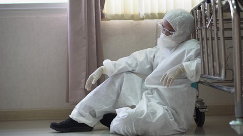 tired doctor wearing ppe suit take a break near bed after hard work feeling worry and sad  in operating room at hospital. exhausted and desperate  surgeon of Coronavirus pandemic  of covid 19 outbreak