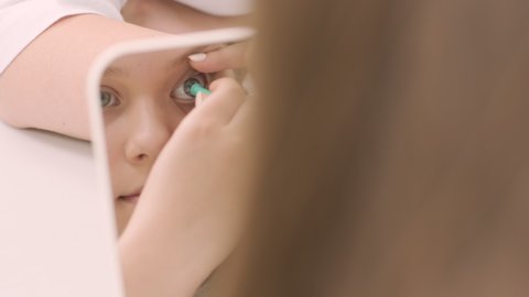 Young girl place the contact lens in the front from the mirror with doctor. Inserting contact lens. Night time contact lenses