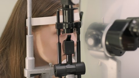 Ophthalmologist check eyesight of young teen with modern equipment. Doctor checking eyes with biomicroscope device. Dolly shot of female doctor examining eye structure with help of medical equipment