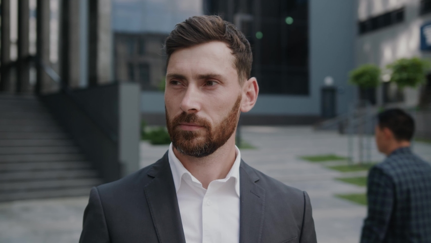 Portrait of handsome businessman standing look at camera smiling near business center. Successful in suit boss company confident. Slow motion