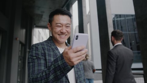 Happy Asian businessman stand smiling use phone near business center. Portrait suit career male young office handsome technology. Slow motion