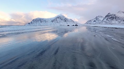 Winter Norway. Deserted wide beach between snow-capped mountains. A surf wave rolls over the sand