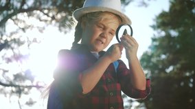 kid tourist examines pine cone with a magnifying glass in park. travel tourism adventure concept. little kid dream boyscout girl with backpack studies nature plant looks through magnifying glass - Powered by Shutterstock - Get 15% off with code: PIKWIZARD15