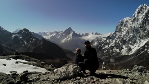 Nepal, Everest Region.   Three passes trek.  Cho La Pass.  Drone video moving up and backwards, Ama Dablam,  high mountain peaks and green lake in background, two hikers, woman and male in foreground.