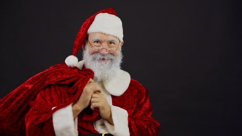 Medium studio shot in slow motion of shocked Santa Claus pulling Christmas sack trying to take gifts away from somebody and finally smiling at camera and walking away with presents