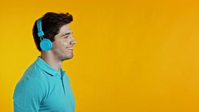 Copy space. Handsome young man with trendy hairdo having fun, smiling, dancing head with blue headphones in studio against yellow background. Music, dance, radio concept, slow motion