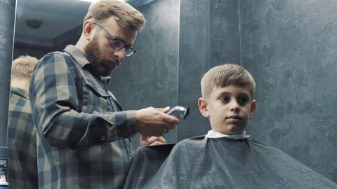 Close-up portrait of a cute handsome caucasian boy sitting barbershop getting his head shaved vintage style haircut professional hairdresser hairstylist barber. healthcare lifestyle