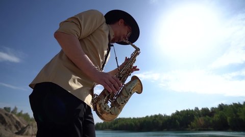 jazz musician is playing saxophone at nature, picturesque landscape at background