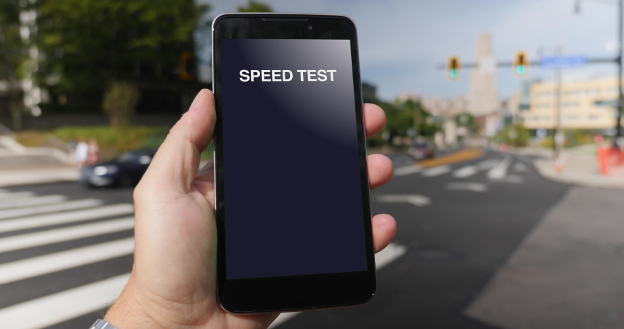 A man in the Oakland district of Pittsburgh tests his cellular download bandwidth speed on a mobile phone. Traffic and taxi cabs pass in background. Fictional interface speedometer gauge created  Royalty-Free Stock Footage #1059734102