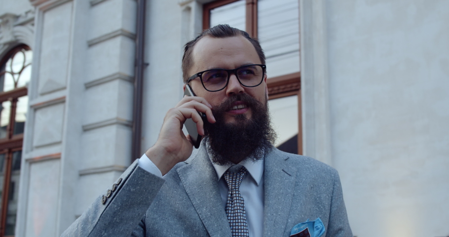 A businessman with a beard and glasses, holds the phone in his hand. A man on the city streets. | Shutterstock HD Video #1059734621