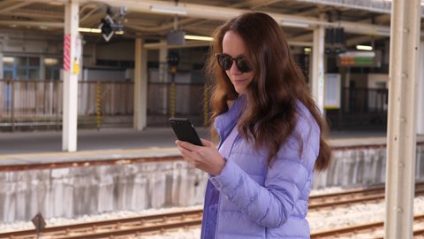 Tourist woman using mobile application, check route and schedule of Japanese rapid transit trains. Lady stand with smartphone at station platform, portrait shot