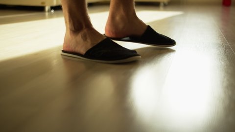 A man in cozy slippers walks on a light floor, camera tracking