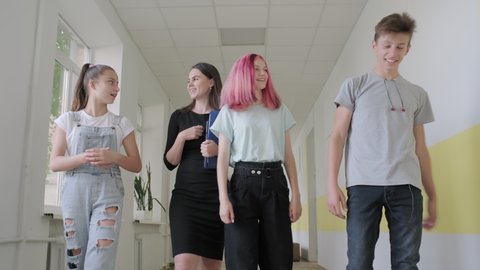 Young female teacher and student teenagers walking down the school hallway smiling and talking. Education, high school, adolescence concept. High quality 4k footage