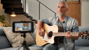 adult man guitarist recording online tutorial using smart phone,mature musician teacher blogger record vlog for his musical class,online lesson blog concept