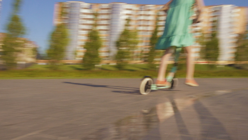 cheerful active child girl riding a scooter in the morning urban park
