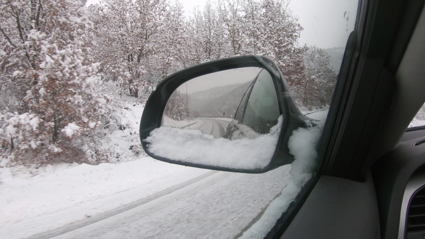 Car driving on snow-covered snowy mountain road in winter snow. Driver`s point of view viewpoint looking through side mirror