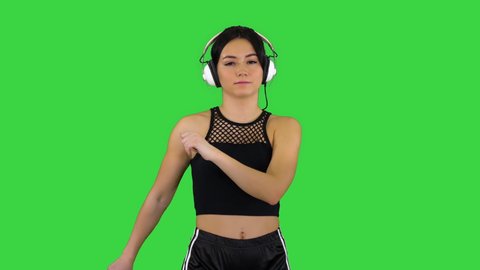 Young happy sportive woman listening music in headphones and dancing on a Green Screen, Chroma Key.