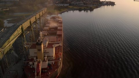 Aerial drone footage of a industrial grain elevator and a cargo ship being loaded in the port of Vancouver at sunset. 4K 24FPS.