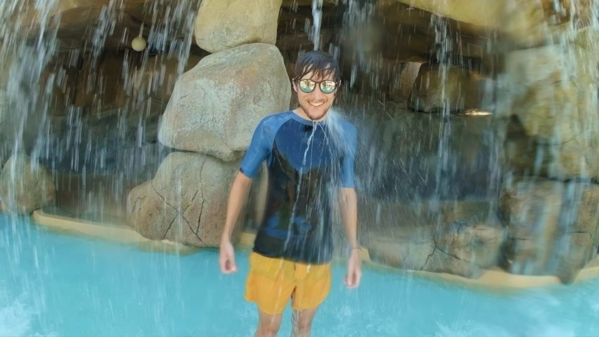 A happy young man is standing under an artificial waterfall in a spa center