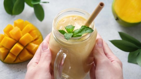 Healthy mango smoothie in glass jar. Woman put fresh smoothie on table