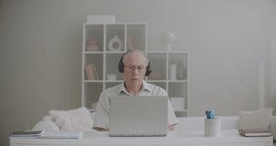 aged male teacher is giving lectures online, staying home, using laptop with internet connection and headphones