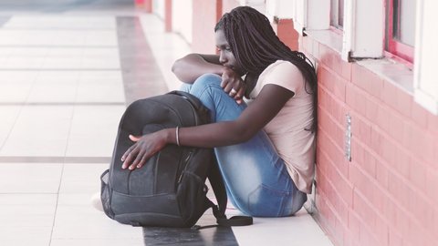 Sad african teenager seated in the school hallway thinking about her problems