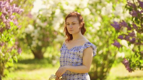 Romantic young woman stands in lilac field and holds white flower thinking about love