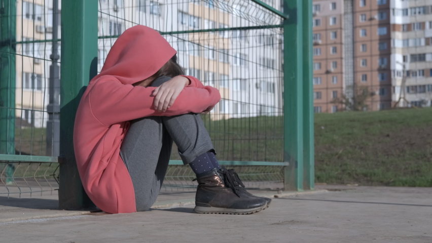 The child is depressed. Childhood loneliness. A depressed girl sits on the floor in the street. Royalty-Free Stock Footage #1059774677
