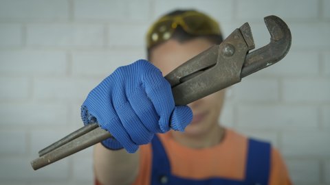 Plumber with a wrench. A smiling woman in uniform in worker gloves hold a wrench in her hand.