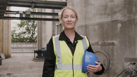 Portrait of female industrial worker looking at camera wearing high vis vest and holding hard hat helmet