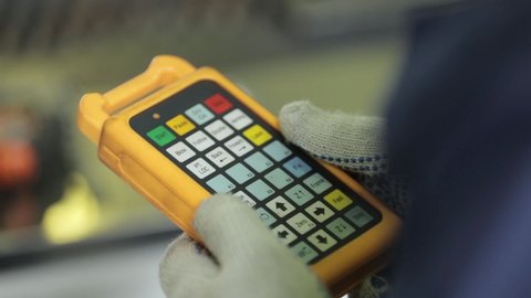 professional engineer in jumpsuit and gloves presses buttons on automatic machine remote control block in yellow plastic case closeup