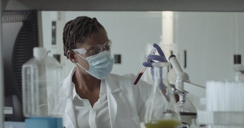 Black Female Laboratory Scientist Conducts Experiment in Science lab looking at blood sample with Coronavirus