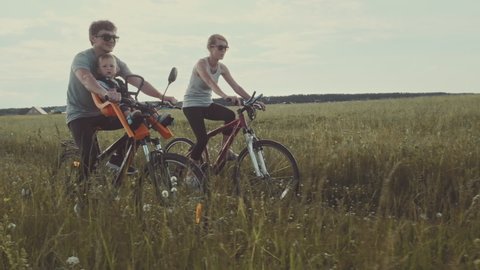 Family cycling outdoor. Young family cycling with baby on a green summer field. : vidéo de stock