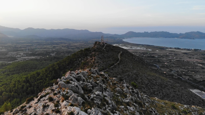 Aerial Over Ridge Line On Forested Hill With Mountains And Lake In Background