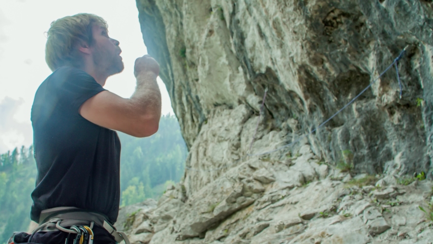 Handsome man rock climber stands, looks up and chalks hands, close up