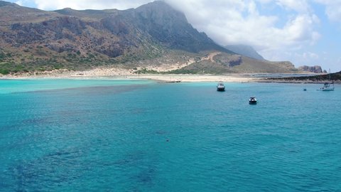 Balos Beach blue waters in Crete Greece with tourist transport ship and it's dinghy boat tied, Aerial flyover reveal shot