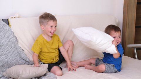 happy laughing siblings having a pillow fight in bed at home