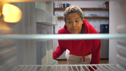 Disappointed African Woman Looking Inside Empty Refrigerator. View from inside of hungry young afro girl opening empty fridge looking for snack and feeling upset