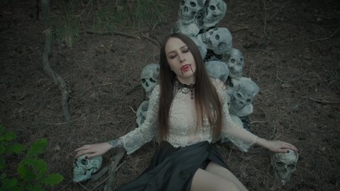 portrait of a young woman vampire, beautiful red lips with dripping blood drops on her face, sharp false fangs. A model in a dark gothic forest against the backdrop of the scenery of human skulls.