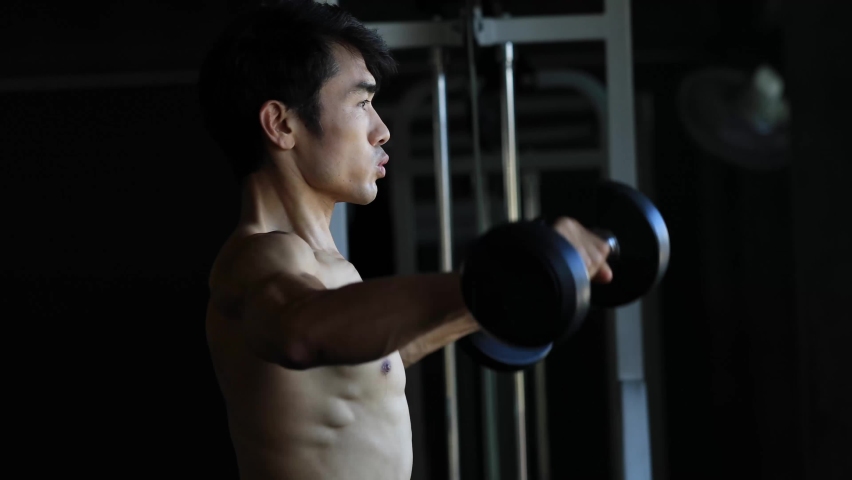 Asian shirtless sporty muscular bodybuilder man excercise with weights building his back muscle in professional sport gym. Bodybuilder lifts dumbbell.