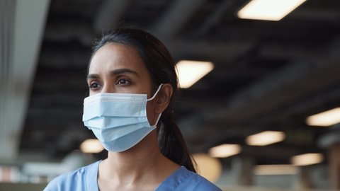 Portrait of smiling overworked nurse in scrubs taking off face mask during break in busy hospital during health pandemic - shot in slow motion