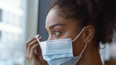 Portrait of overworked nurse in scrubs putting on face mask taking break and looking out of window in busy hospital during health pandemic - shot in slow motion