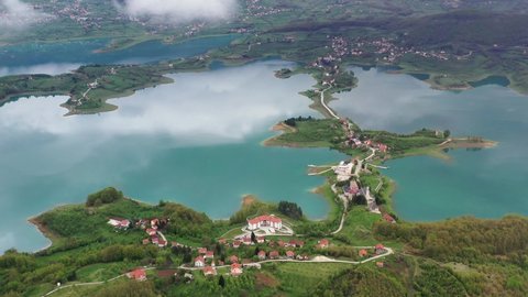 Sensational scenic view of green lake Rama water toward picturesque small island village community, Prozor-Rama, Bosnia and Herzegovina, overhead aerial approach