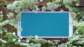 Top view flatlay 4k video footage of smartphone blue screen mock up and flowers. Floral pattern around phone.  Spring or summer background with mobile cellphone with copy space. - Powered by Shutterstock - Get 15% off with code: PIKWIZARD15