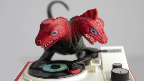 Footage of plastic toy dinosaur with two heads playing records on decks
